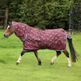 A horse wearing a teal horse rug with a cartoon horse pattern, trotting in a grassy field with trees in the background.