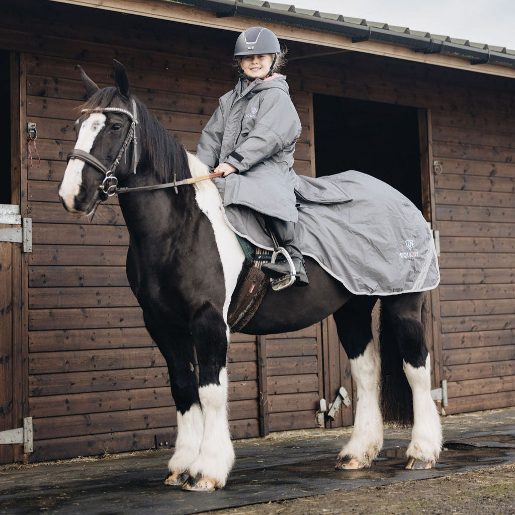 Person riding a horse in front of a wooden stable