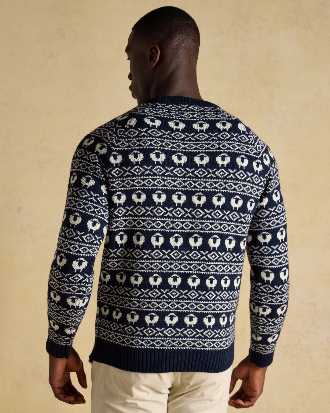Man wearing a navy blue sweater with white sheep pattern on a beige background