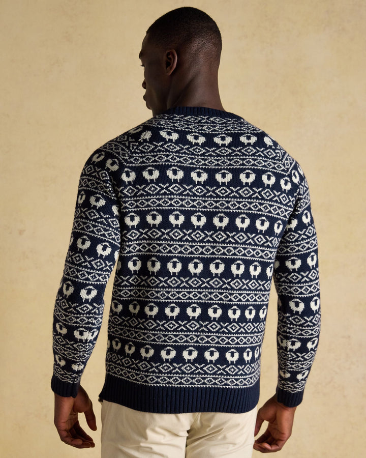 Man wearing a navy blue sweater with white sheep pattern on a beige background