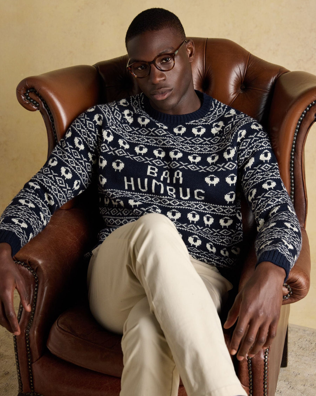 Man wearing a sweater with 'Baa Humbug' text, sitting in a leather armchair.