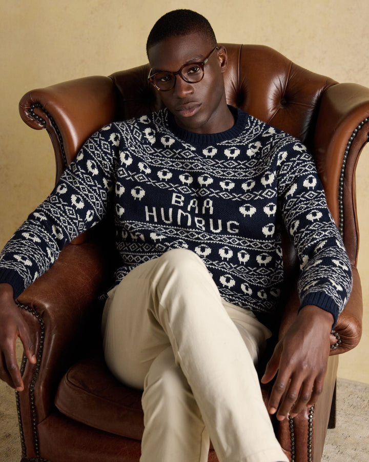 Man wearing a sweater with 'Baa Humbug' text, sitting in a leather armchair.