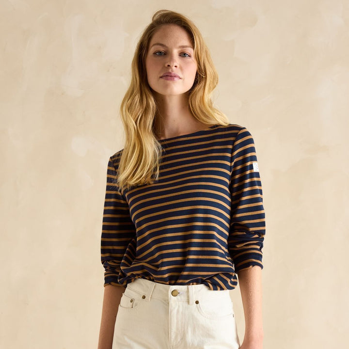 Woman wearing a striped shirt and white pants against a beige background