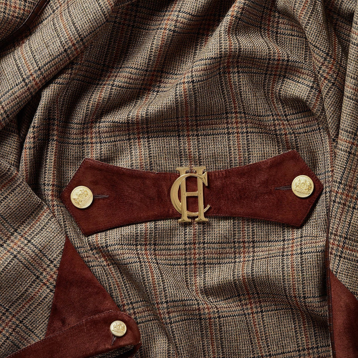 Close-up of a brown plaid cape with a wide brown suede belt featuring a gold-tone interlocking HC logo and gold buttons.
