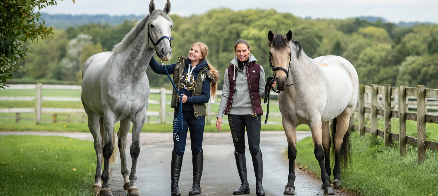 Two women wearing equestrian clothing with two horses