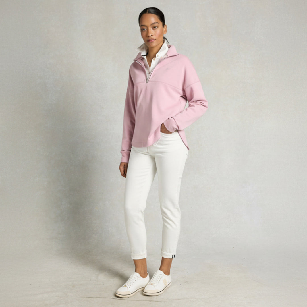 Woman wearing a pink sweater and white pants against a gray background