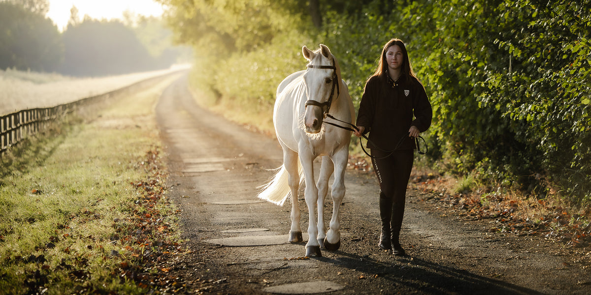 Woman in new Holland Cooper clothing leading a horse down a lane