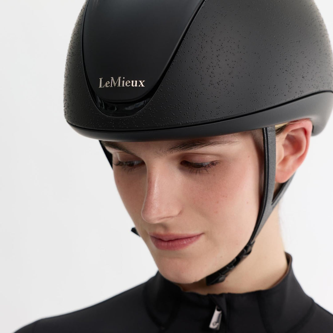 Person wearing a black LeMieux helmet on a white background