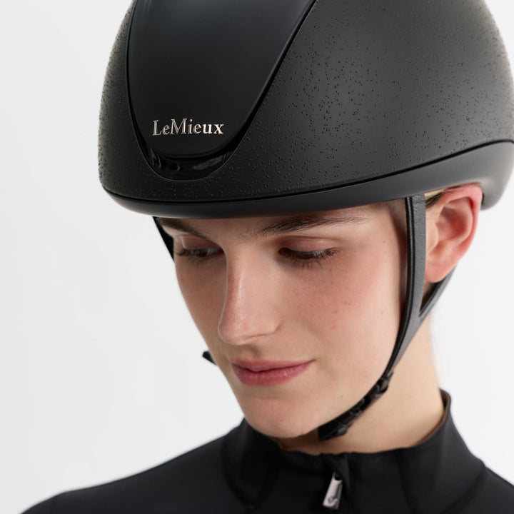 Person wearing a black LeMieux helmet on a white background