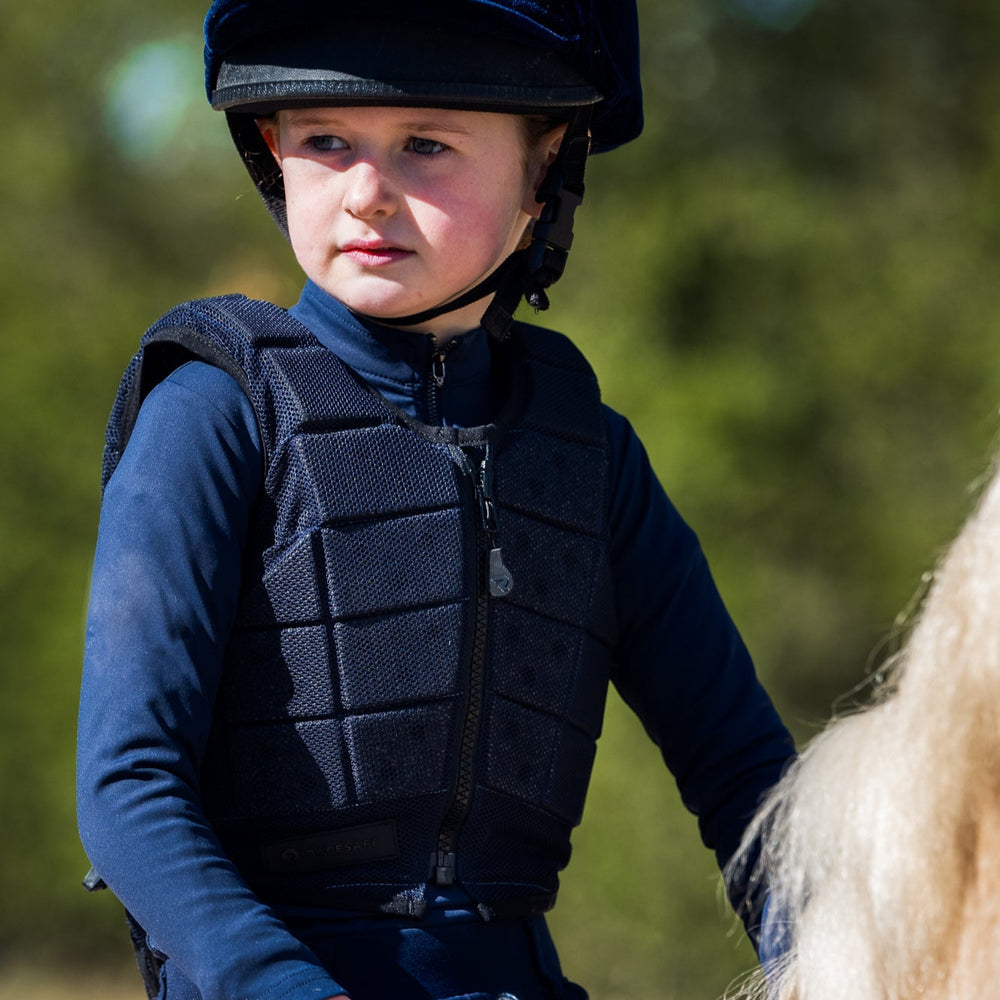 Child in equestrian gear sitting on a horse with a blurred natural background