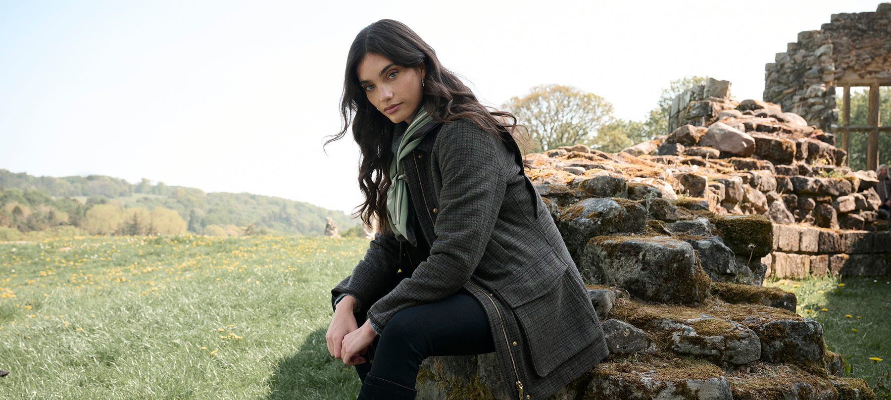 Woman sitting on a stone wall wearing new Fairfax & Favor