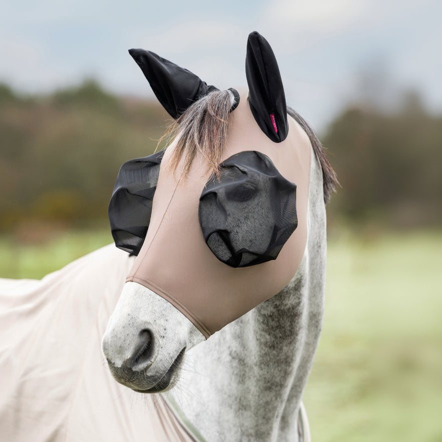 Horse wearing a black & beige fly mask with ear holes in an outdoor setting